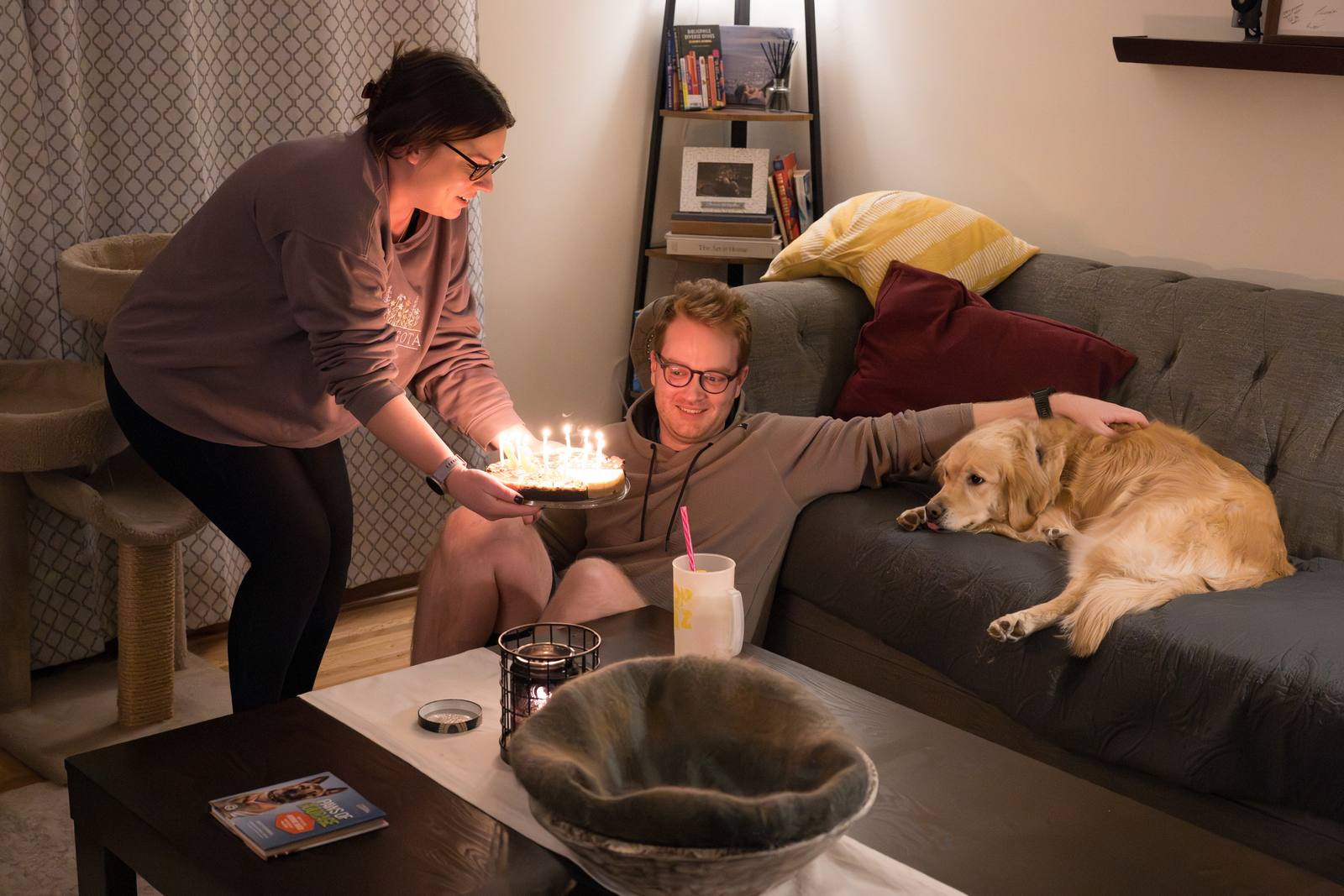 People relaxing in a living room while a dog rests on the couch.