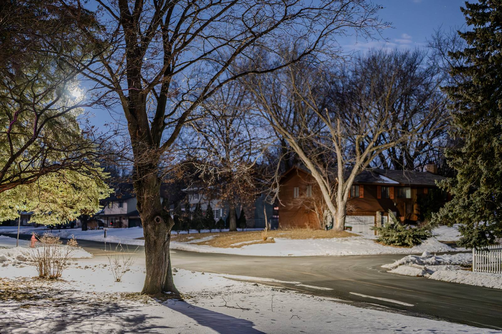 A snow-covered residential street lined with bare trees.