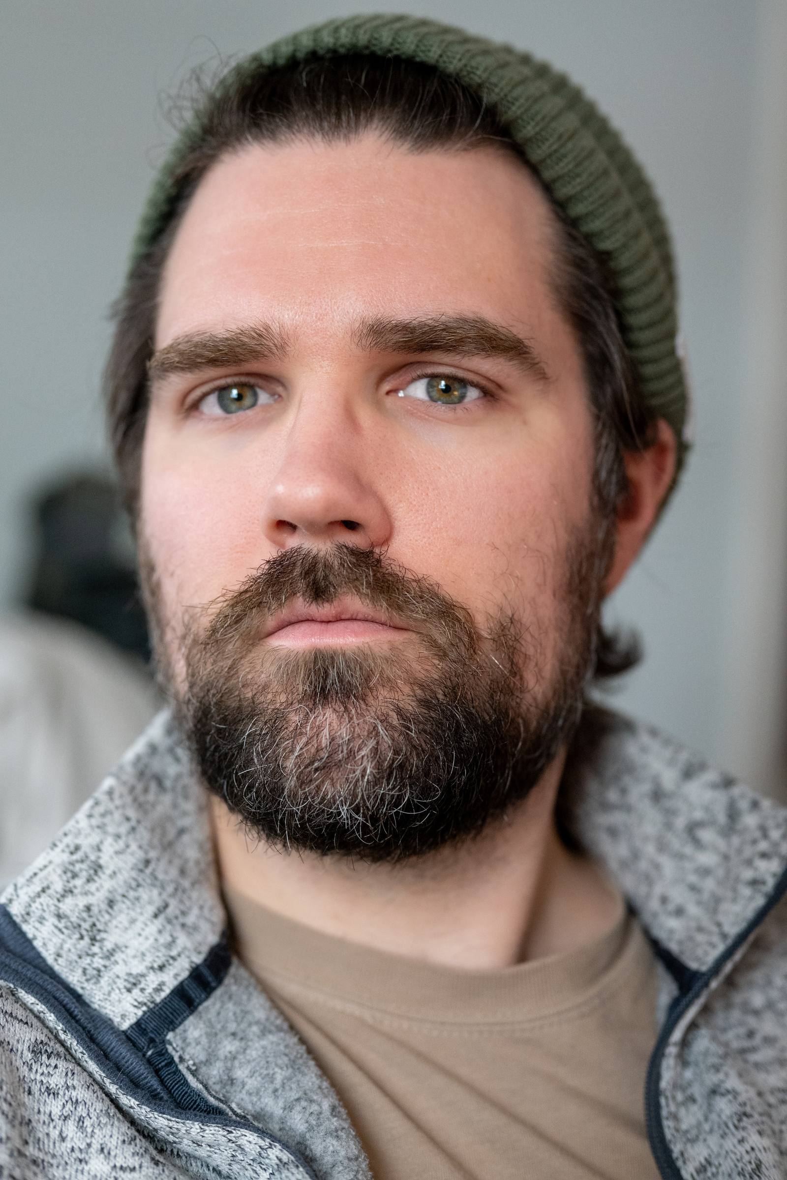 A close portrait of a bearded person wearing a dark knit cap.
