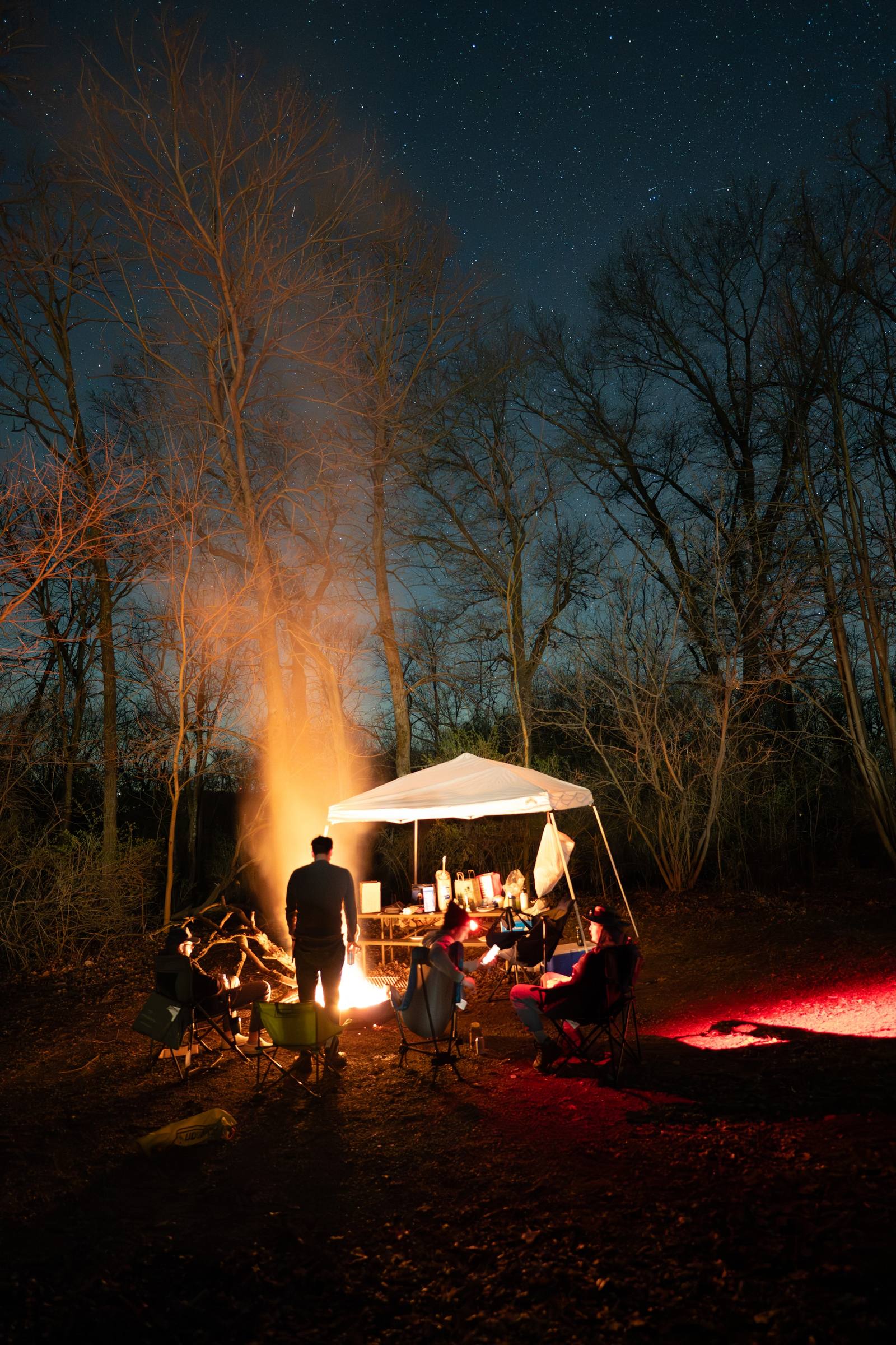 A small campsite glows under bare trees at night.