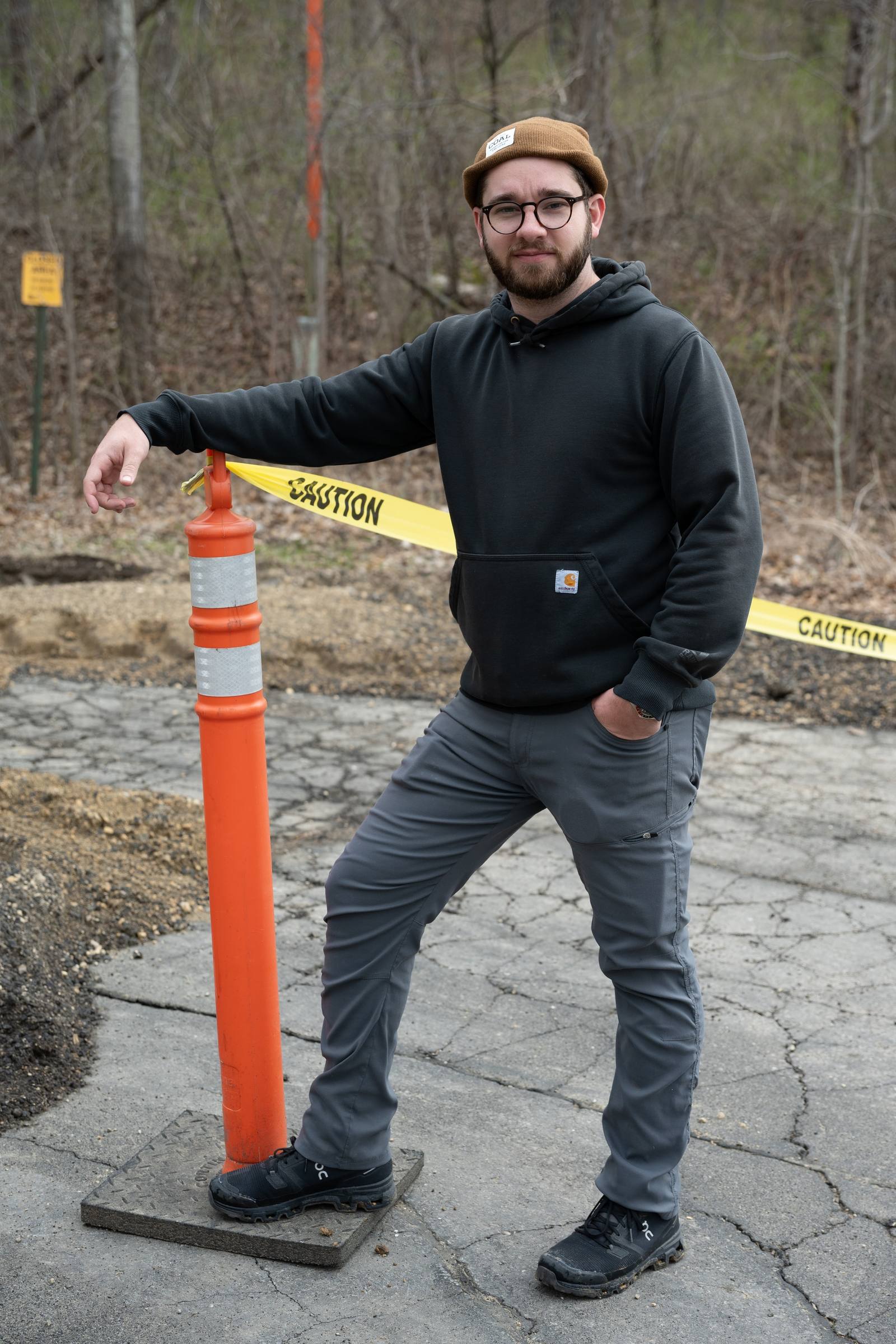 A man stands near an orange traffic cone on a wooded path.